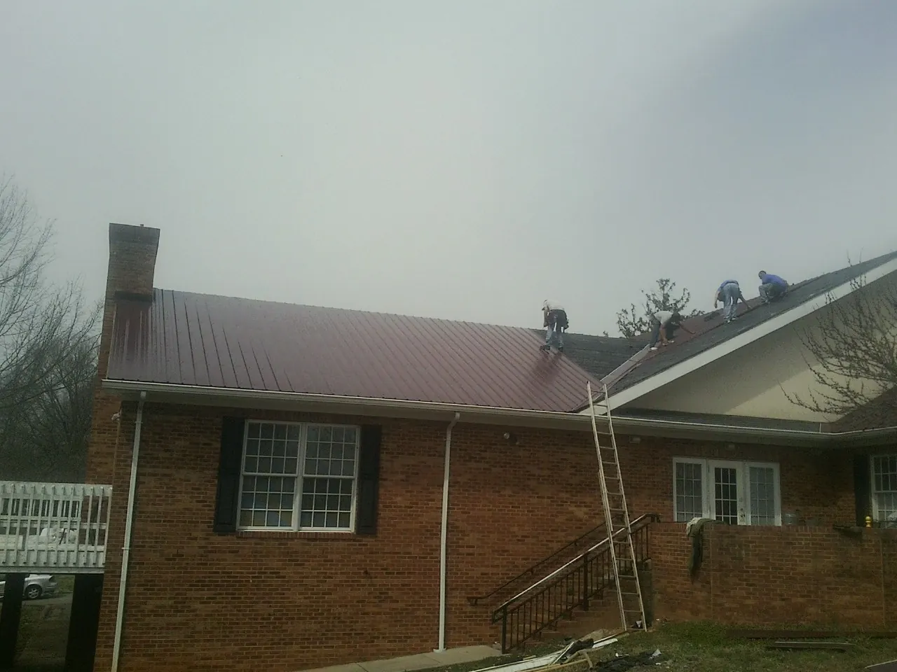 Crew setting red metal roofing panels on a brick home in Greenfield